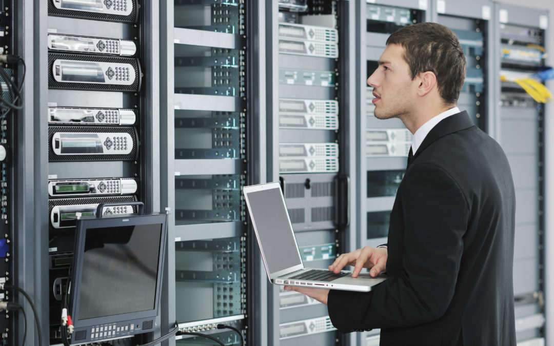 Engineer in business suit with laptop in network server room